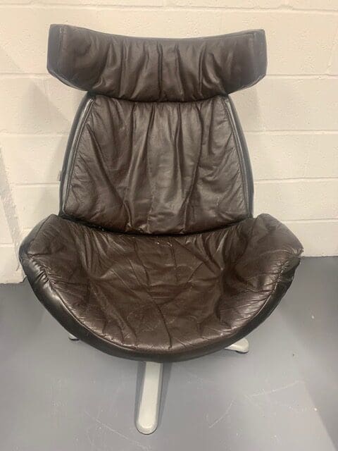 A brown leather chair sitting in front of a white wall.