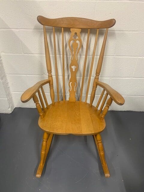 A wooden rocking chair sitting in front of a white wall.