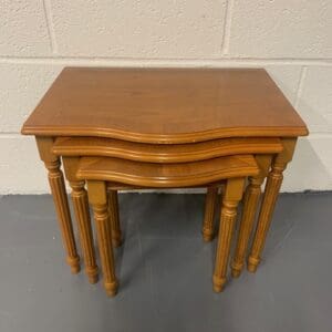 A set of three wooden tables with one has a top that is bent.