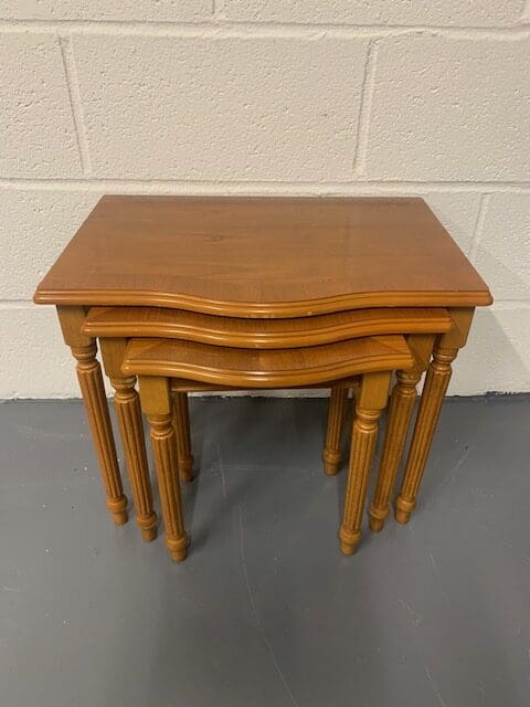 A set of three wooden tables with one has a top that is bent.