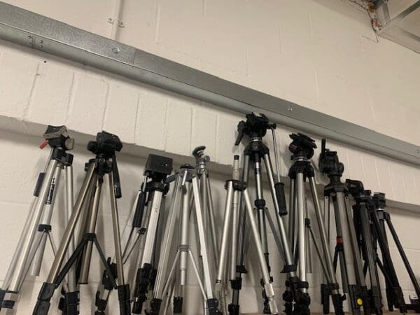 A wall of different types of tripods hanging on the side.