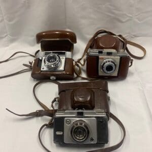 Three cameras are sitting on a table with one of them open.