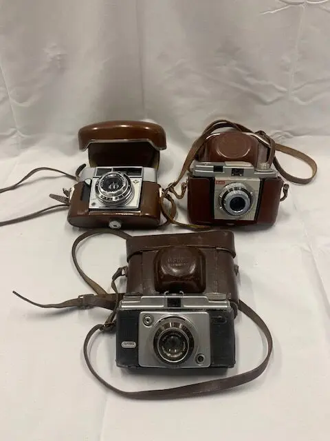 Three cameras are sitting on a table with one of them open.