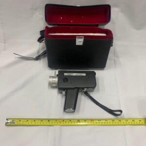 A small camera and a measuring tape in front of a red case.