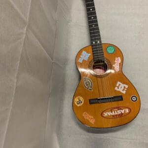 A guitar with stickers on it sitting on top of a bed.