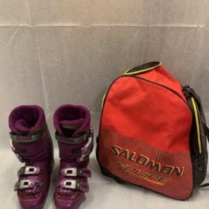 A pair of purple ski boots next to a red backpack.