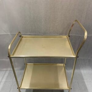 A gold metal cart with two shelves and handles.