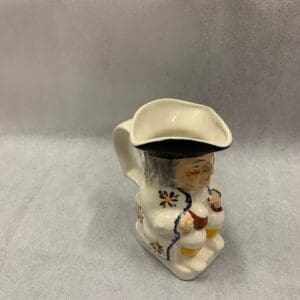 A small white pitcher with a hat on it