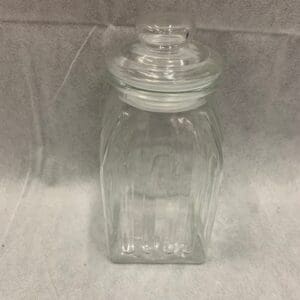 A glass jar with a lid on the ground.