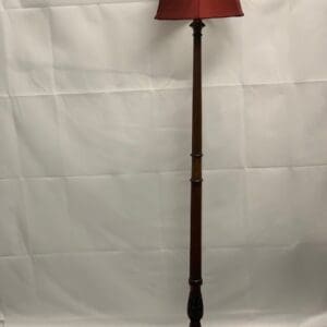 A wooden floor lamp with red shade on top of it.