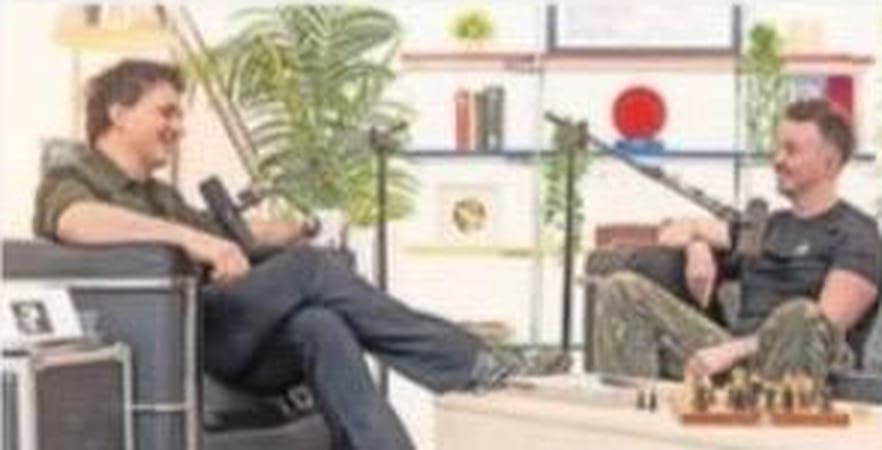Two men chatting in an interview setting on hired sofa and armchair from House Of Props, with a plant and shelves behind them